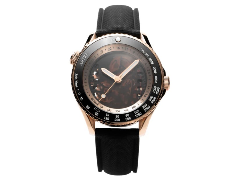 Un reloj de lujo con correa de cuero negro, caja de oro rosa, bisel negro y dorado y esfera translúcida que deja ver los engranajes internos del reloj. Hay varias marcas de medidas en el bisel.