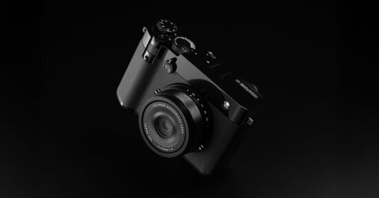 A sleek, black digital camera with a lens and various control dials is displayed on a dark background, showcasing its modern and minimalist design.