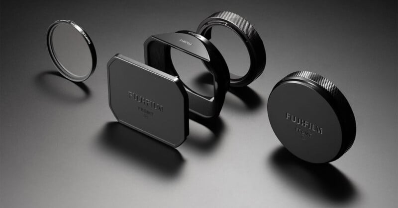 Cinco accesorios para lentes de cámaras Fujifilm, incluidas tapas de lentes, filtros y parasoles, están alineados sobre una superficie oscura con una iluminación espectacular que resalta sus acabados metálicos y mate.