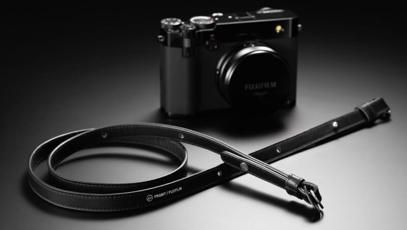 Cámara digital Fujifilm negra sobre una superficie oscura con correa de cuero negro rizado etiquetada "cámara frontal fujifilm," Colocar en primer plano. La cámara y la correa están iluminadas con una iluminación suave y dramática.