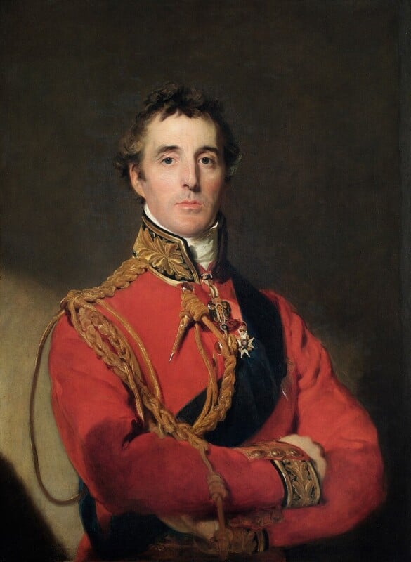 A formal portrait of a man in a red military uniform with gold detailing and medals, standing with arms crossed against a dark background.