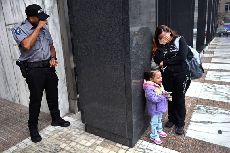 Un guardia de seguridad observa cómo una mujer se cubre la cara y llora junto a una niña en una acera de la ciudad. La escena parecía tensa y emocionante.
