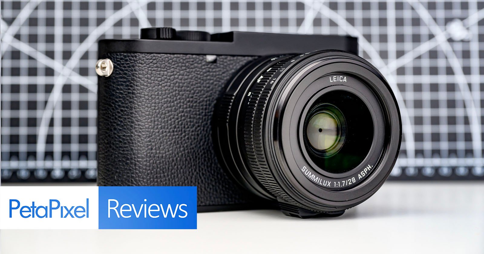 A Leica digital camera with a large lens is displayed on a surface, in front of a geometric black-and-white background. The image includes "PetaPixel Reviews" text in the lower left corner.