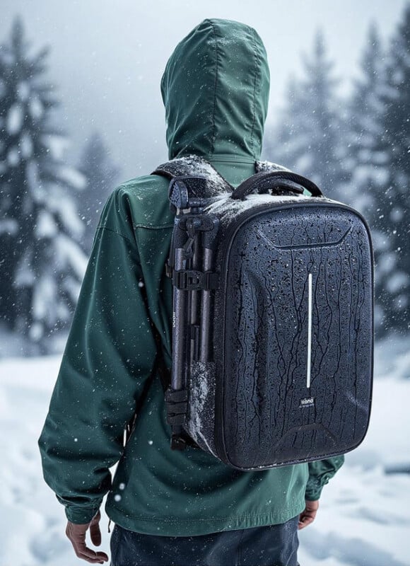 A person in a green jacket and hood stands in a snowy forest, seen from behind, wearing a black, waterproof backpack covered with water droplets and snow. Pine trees and snowflakes fill the wintry background.