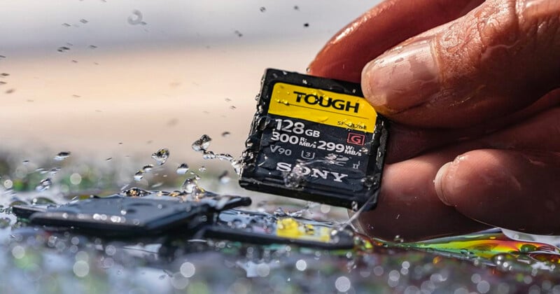 A hand holds a wet Sony Tough 128GB SD card above a surface with water droplets and another SD card, highlighting the card’s water resistance and durability.