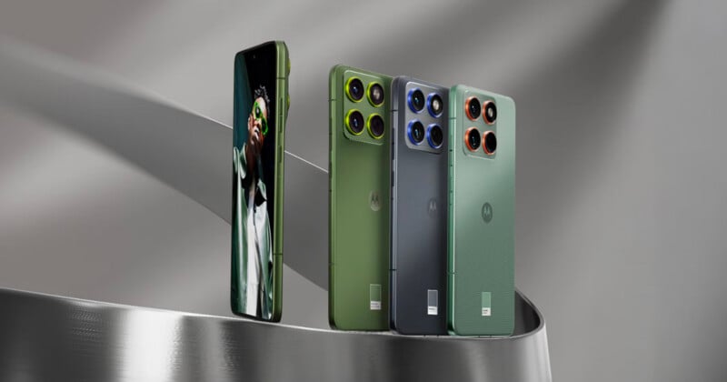 Cuatro teléfonos inteligentes Motorola se muestran sobre una superficie metálica curva; tres de ellos lucen sus elegantes diseños traseros en verde, azul y verde grisáceo, mientras que uno luce su frente con un retrato en la pantalla.