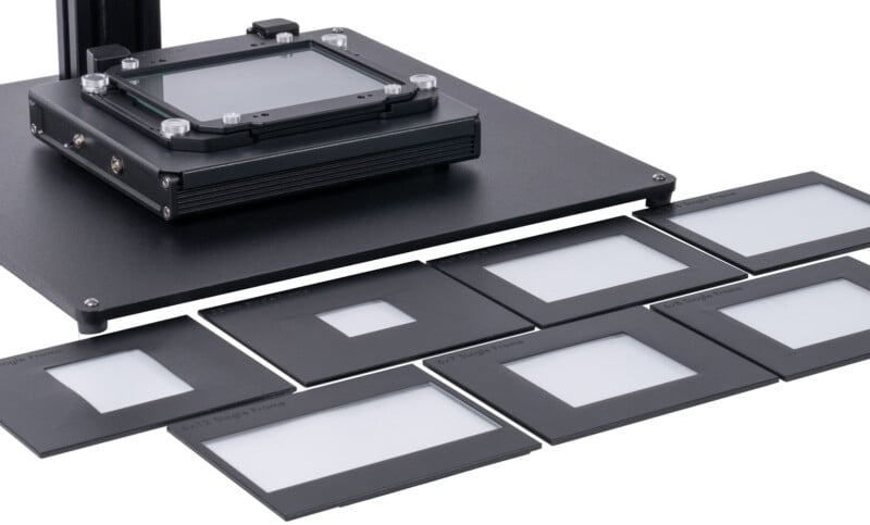 A close-up of a flatbed scanner with several glass slide holders arranged around it, each containing empty white surfaces, ready for scanning.