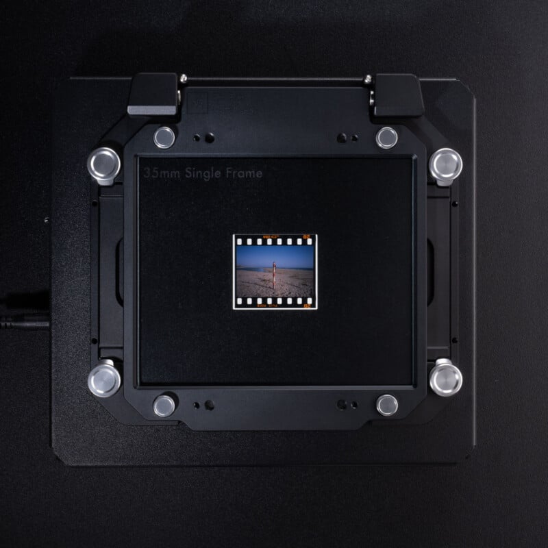 A 35mm film slide with a landscape image is mounted in a black, square film scanner holder marked "35mm Single Frame," set against a dark background.