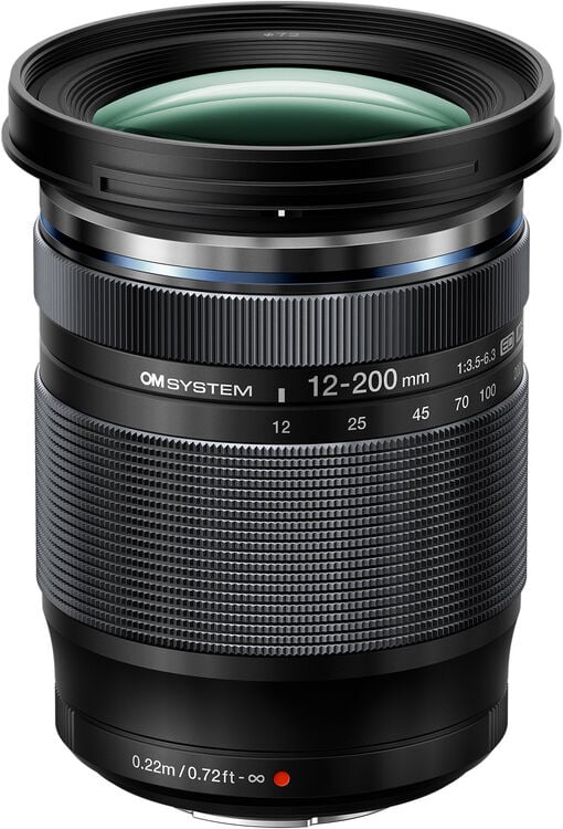 A close-up of a black OM System 12-200mm camera lens, showing detailed focus and zoom rings, lens markings, and a green-coated front glass element.