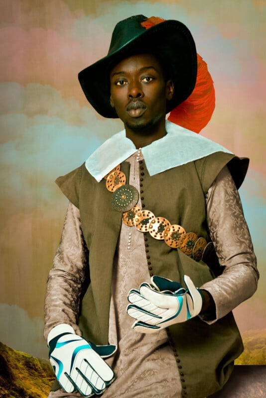 A person in a historical costume with a feathered hat and large collar poses against a scenic backdrop, wearing modern sports gloves and a decorative belt.