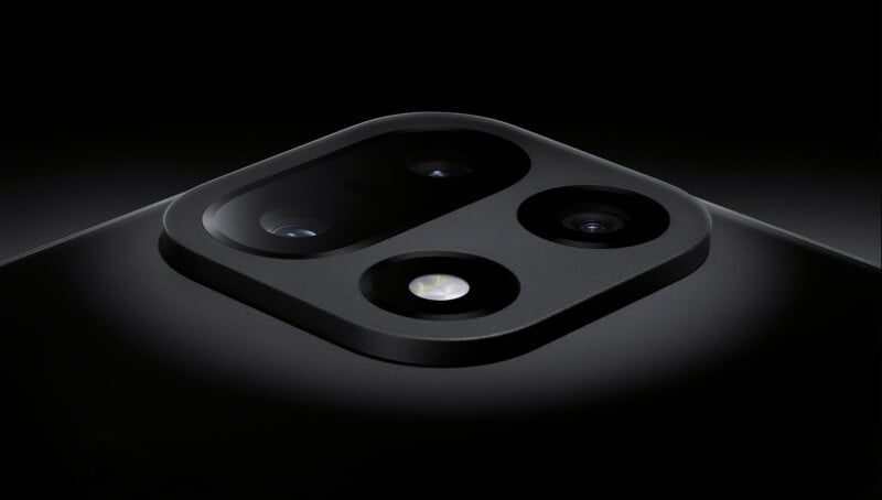 Primer plano del módulo de cámara trasera del teléfono inteligente negro que muestra tres lentes de cámara y flash sobre una superficie mate lisa sobre un fondo oscuro.