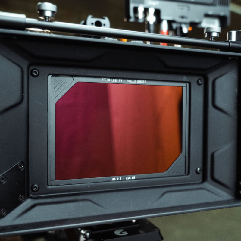 Primer plano de la pantalla del monitor de la cámara con un tinte rojizo rodeado por un marco negro sólido y varios controles que indican equipos de video o filmación profesionales.