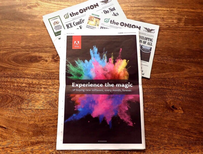 A colorful Adobe ad in a newspaper features a vibrant powder explosion and the text "Experience the magic of buying new software, every month, forever." Two issues of The Onion newspaper are partially visible underneath.