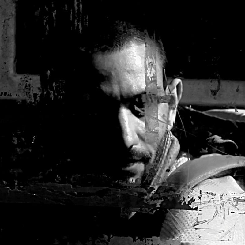 A black and white image of a man with a serious expression, partially obscured by dark, abstract textures and scratches, creating a moody and mysterious atmosphere.