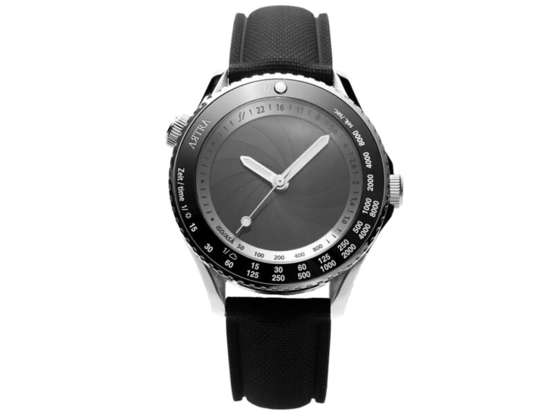 Reloj plateado con correa texturizada negra, esfera gris, agujas de horas y minutos plateadas, bisel marcado con varios números y unidades. marca "asreya" Visible a la izquierda.