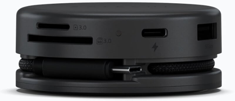 Un dispositivo electrónico compacto, redondo y negro con una variedad de puertos, incluidos USB, USB-C, ranuras para tarjetas microSD y SD, y un cable enrollado cuidadosamente enrollado alrededor de la base.