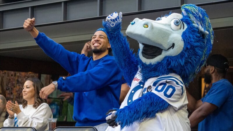 Un hombre con una camisa azul y una gran mascota de un caballo azul que lleva una camiseta de los Indianapolis Colts animan con entusiasmo en un evento deportivo, rodeado de otros fanáticos.