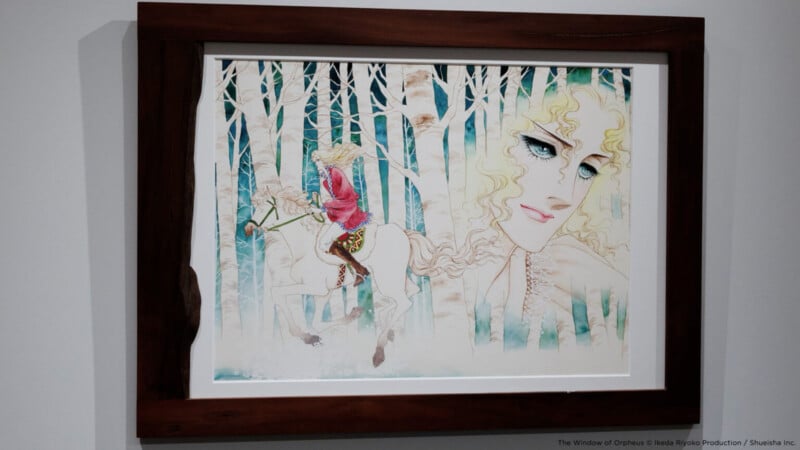 Una obra de arte enmarcada muestra a un hombre rubio montando un caballo blanco a través de bosques blancos, con otro hombre al fondo con un rostro grande y etéreo, ojos azules y cabello rizado.