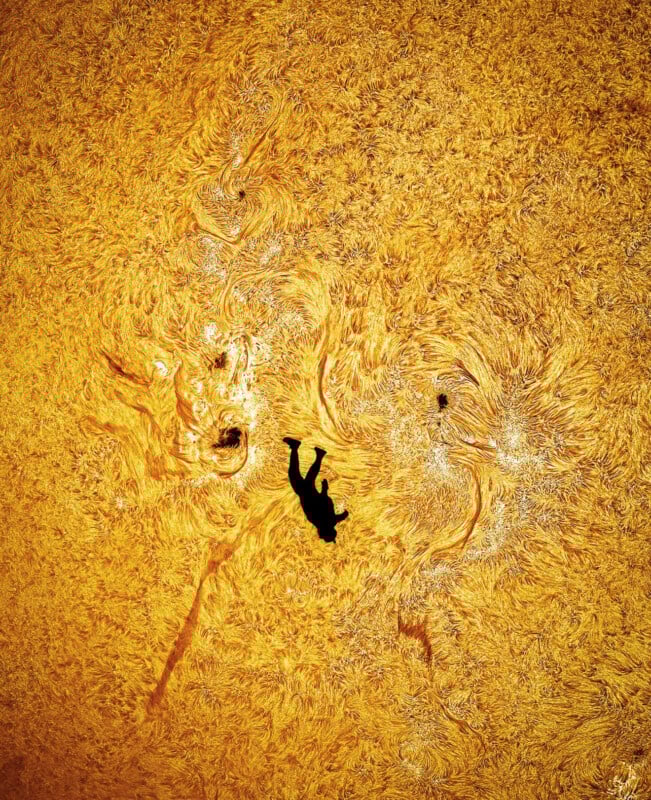 A black silhouette of a person appears to be floating or falling against a swirling, textured golden-yellow background resembling the surface of the sun.