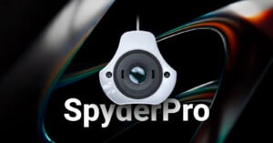 A close-up of a SpyderPro calibration device hanging against a dark, abstract background, with the word "SpyderPro" in bold white text below.