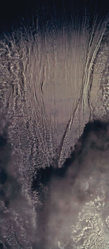 An aerial view of cloud formations over dark ocean water, with wispy, textured clouds and streaks creating abstract patterns in shades of gray, white, and brown.