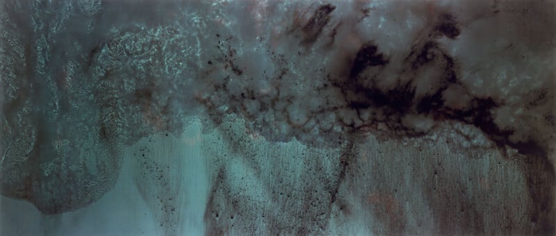 Aerial view of Mars’ south pole showing dark streaks and swirling patterns of ice, frost, and dust, creating a cloudy, textured landscape with varying light and dark patches.