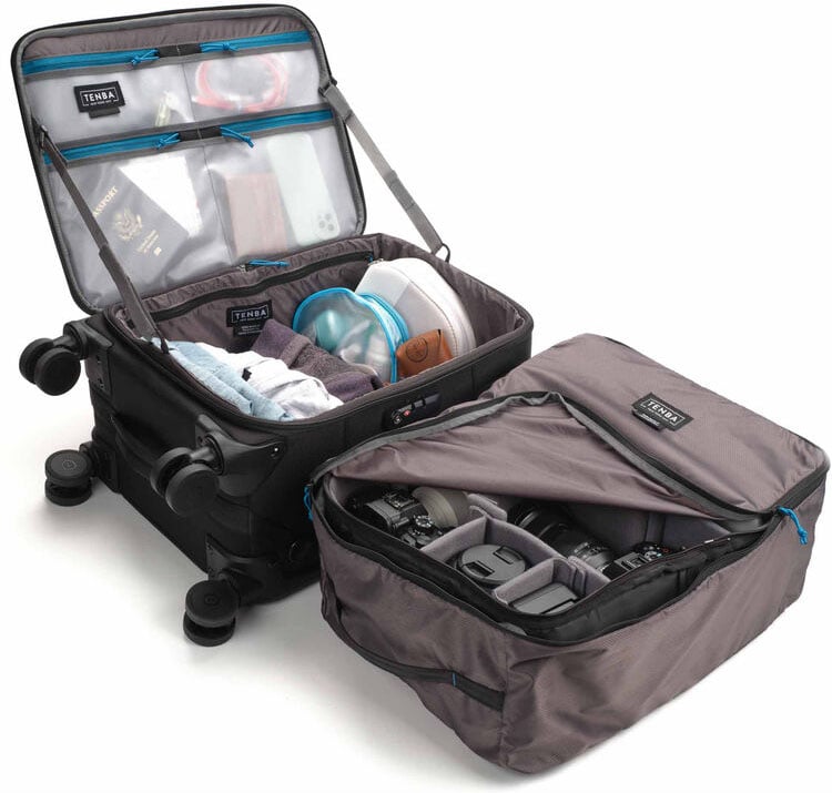 Dos maletas abiertas: una que contiene artículos de tocador, ropa y un pasaporte en un bolsillo de malla, la otra llena de equipo fotográfico y lentes en un compartimento acolchado. Ambos bolsos son grises con cremalleras azules.