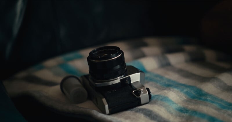 A vintage film camera and a film canister lie on a striped blanket with soft, muted lighting creating a cozy, nostalgic atmosphere.