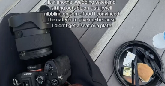 A person with a camera and lens on their lap sits on outdoor steps next to a disposable plate with a half-eaten burger, cheese, and plastic cutlery. Text overlay describes their experience as a wedding photographer without a seat or plate.