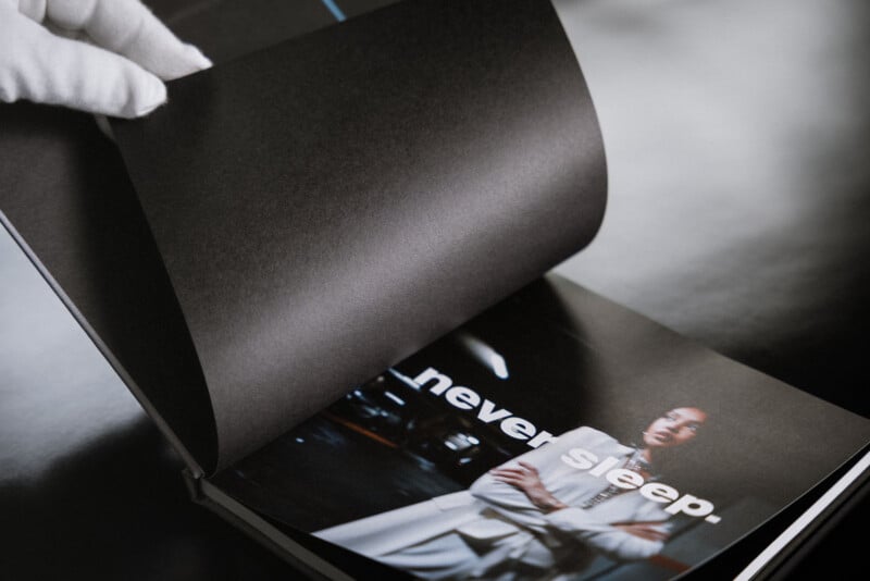 A gloved hand turns a black page in a book, revealing a photo of a person in a white outfit with the words "never sleep." printed over the image.