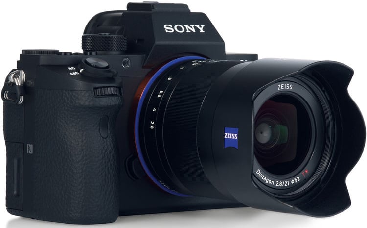 A black Sony digital camera with a large Zeiss lens attached, featuring textured grip and visible control dials, positioned at a slight angle on a white background.