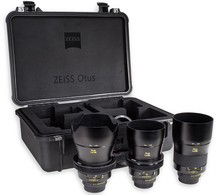 Three Zeiss Otus camera lenses with yellow markings are displayed in front of a black Zeiss-branded hard case with custom foam compartments for lens storage.