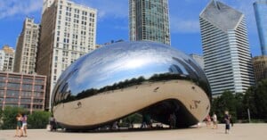 Cloud Gate, also known as "The Bean," a large reflective sculpture in Chicago’s Millennium Park, with skyscrapers and blue sky in the background. People are gathered around and beneath the sculpture.