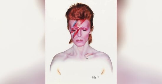 A person with pale skin and bright red hair styled upwards, eyes closed, with a bold pink and blue lightning bolt painted across their face. The background is plain white.