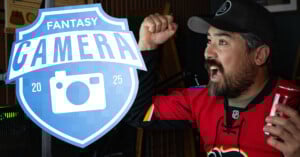 A man in a red hockey jersey and black cap cheers excitedly while holding a can of Coca-Cola. A blue "Fantasy Camera 2025" logo with a camera icon is overlaid on the left side of the image.