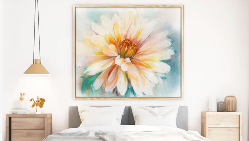 A large, colorful painting of a flower with yellow, orange, and white petals hangs above a neatly made bed in a bright, modern bedroom with light wood furniture and minimal decor.