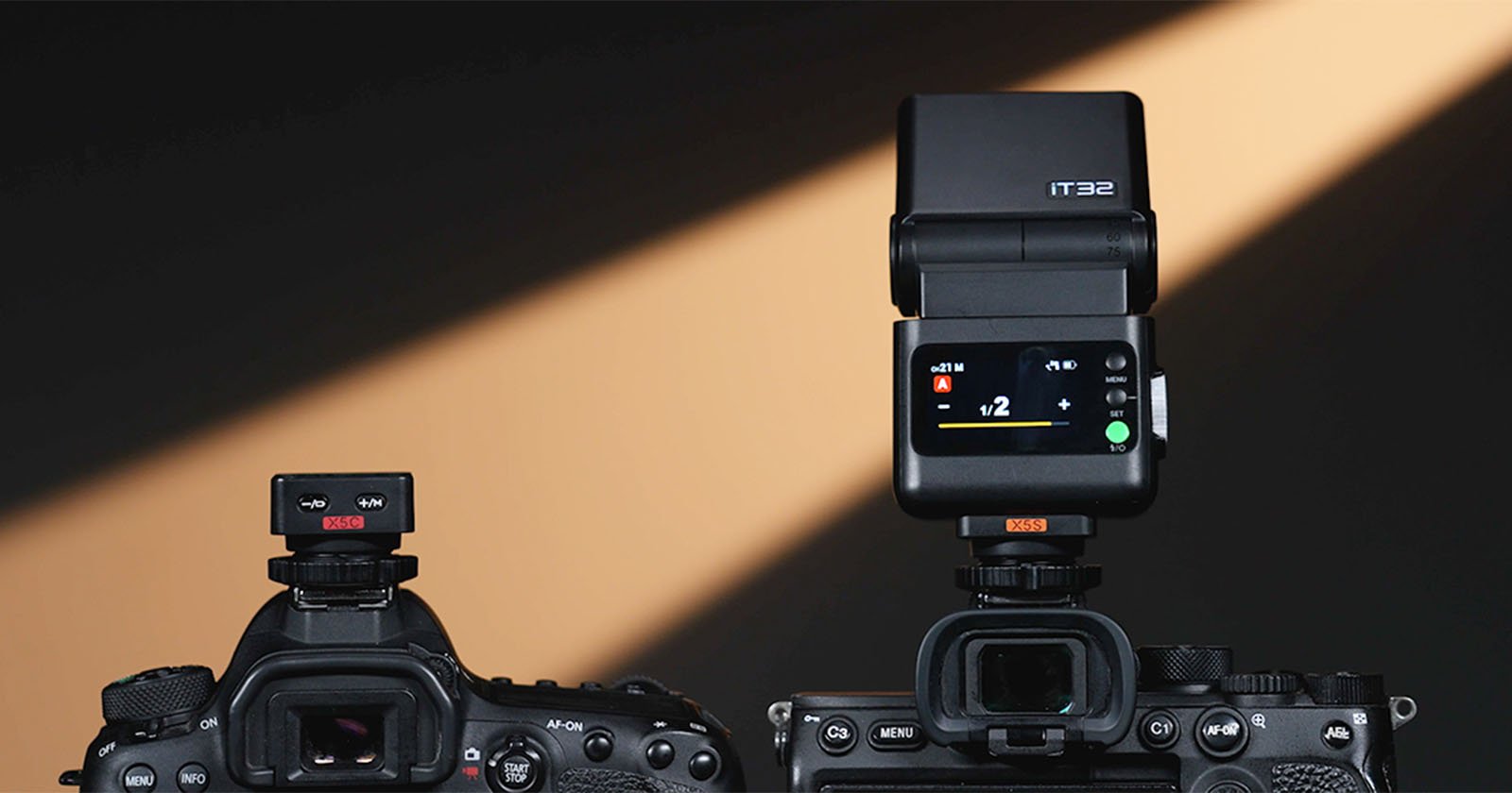 Two digital cameras are shown from the back, each with a device mounted on top. The left camera has a small wireless transmitter, while the right has a larger flash unit with a lit display screen. A dramatic light shines in the background.