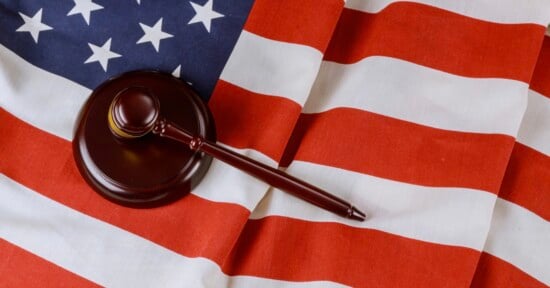 A wooden judge’s gavel rests on the folded American flag, symbolizing law and justice in the United States.