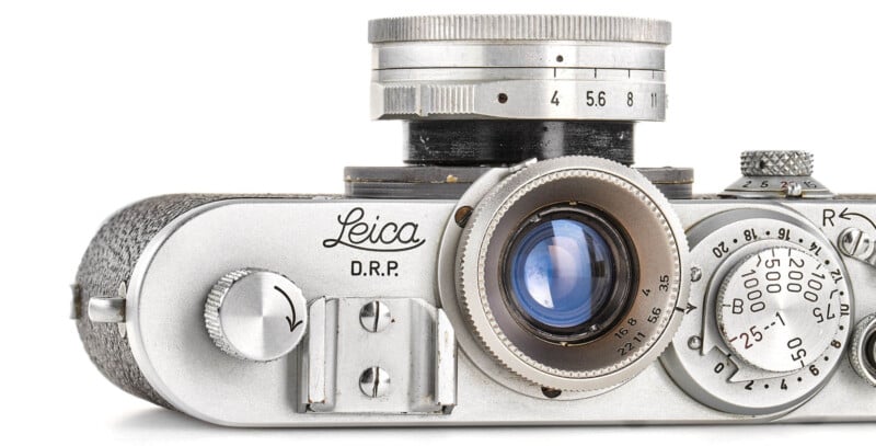Close-up view of a vintage Leica D.R.P. camera, showing the lens, dials, and camera controls on a white background.