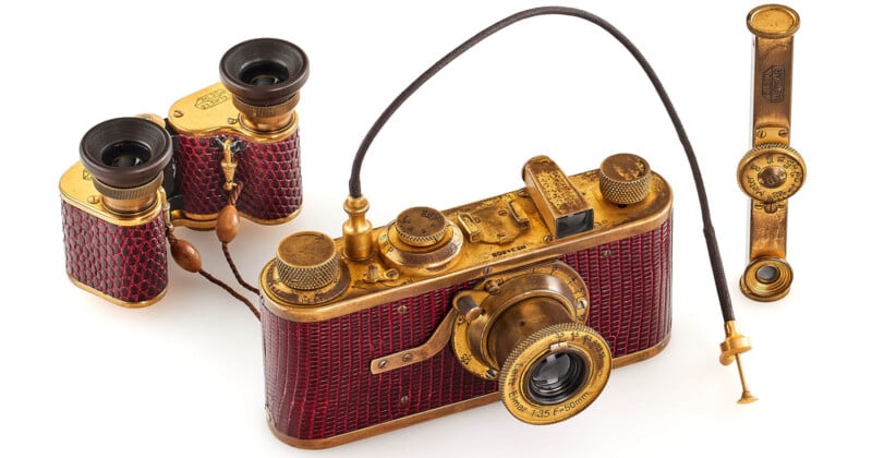A vintage Leica camera set in gold and red leather, accompanied by matching binoculars and a rangefinder, all with a luxurious, ornate design, displayed on a white background.