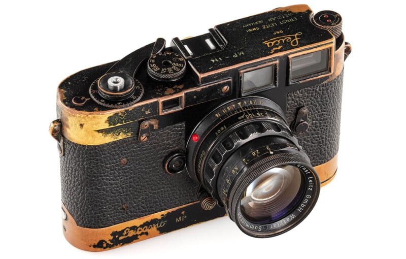 A vintage black and gold Leica MP film camera with visible signs of wear, textured grip, and a mounted lens, viewed at an angle from above.