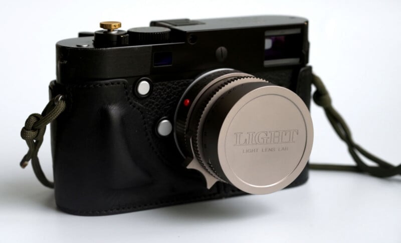 A compact black camera with a textured grip, a metallic lens cap labeled “LIGHT LIGHT LENS LAB,” and a green wrist strap, set against a plain white background.
