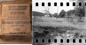A wrapped roll of vintage film labeled “EASTMAN FLUOROGRAPHIC SAFETY FILM” sits beside a black-and-white photo of a rural scene with a house, trees, and a wire fence, bordered by sprocket holes.