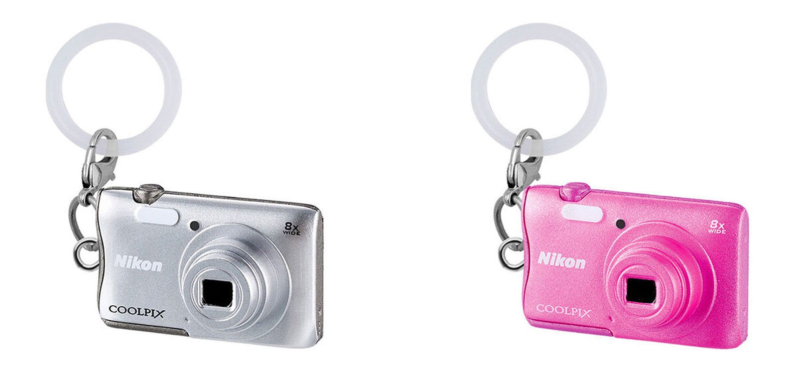 Two keychains shaped like miniature Nikon COOLPIX cameras, one silver and one pink, each with a white circular ring attached to the top left corner.