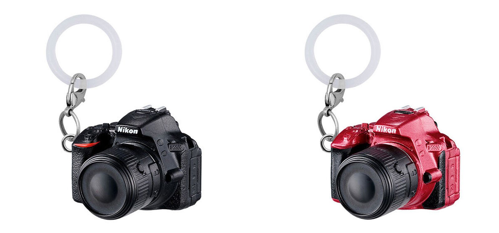 Two keychains shaped like Nikon cameras, one black and one red, are shown side by side against a white background. Each keychain has a round, translucent plastic ring attached.