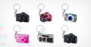 Six miniature camera-shaped keychains in different styles and colors, including black, red, blue with a colorful pattern, pink, silver, and black, arranged in two rows on a white background.