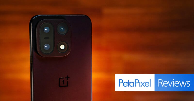 A close-up of a OnePlus smartphone’s rear camera module against a warm, blurred background, with "PetaPixel Reviews" text in a blue and white banner in the lower-right corner.