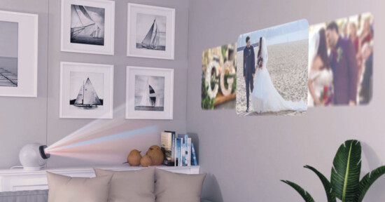 A projector sits on a side table, projecting wedding and couple photos onto a wall above a sofa, which is decorated with framed sailboat pictures and a green plant nearby.