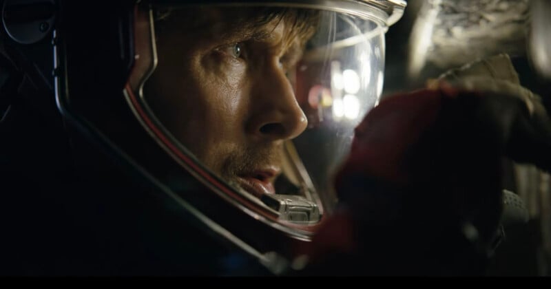 A close-up of a person wearing a space helmet, looking intently forward with light reflecting off the visor and dim surroundings.