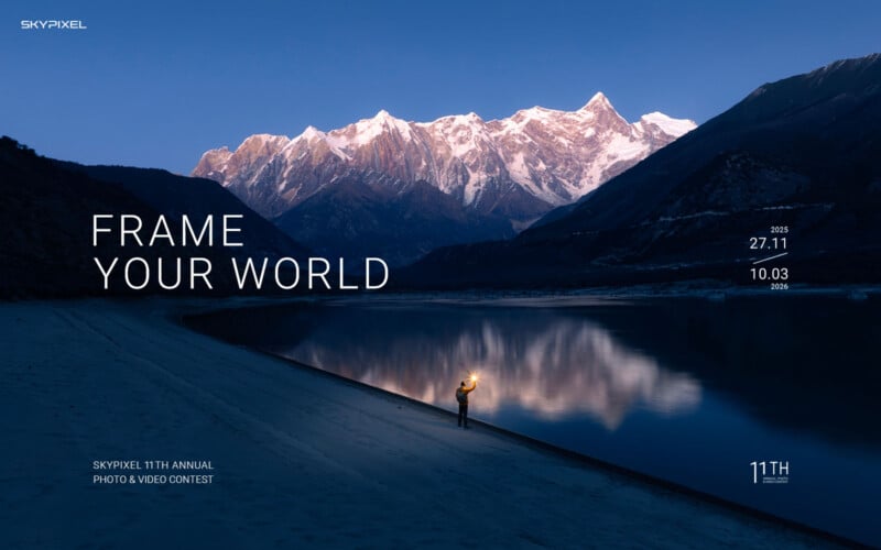 A person holding a lantern stands by a calm lake at dusk, with snow-capped mountains reflecting in the water under a deep blue sky. Text reads "Frame Your World" and details for a photo and video contest.